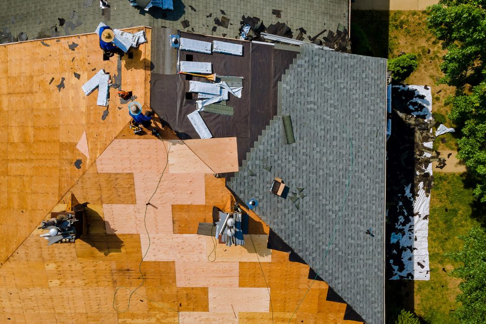 Aerial view of workers installing shingles on a house roof.