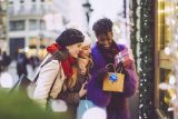 Three women smiling, holding gifts on a festive street; perfect holiday marketing.