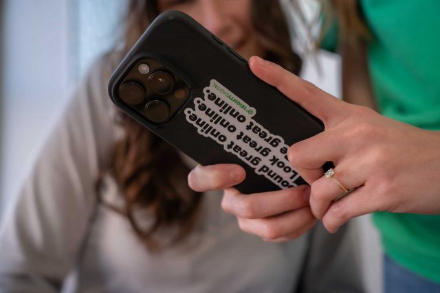 A hand holds a phone with a sticker that says, Look great, feel great, online.