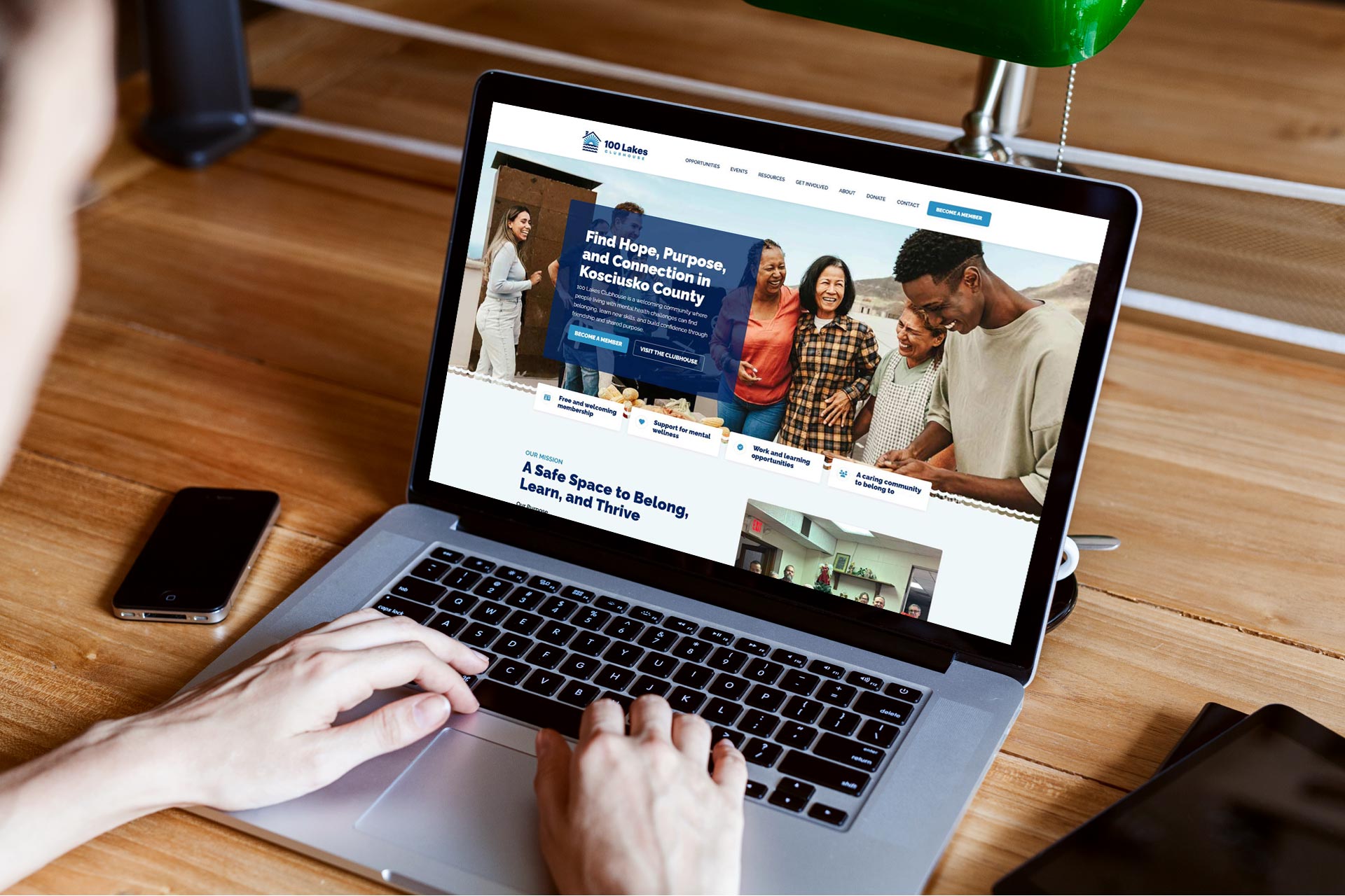 Person using a laptop displaying a community center website at a wooden desk.