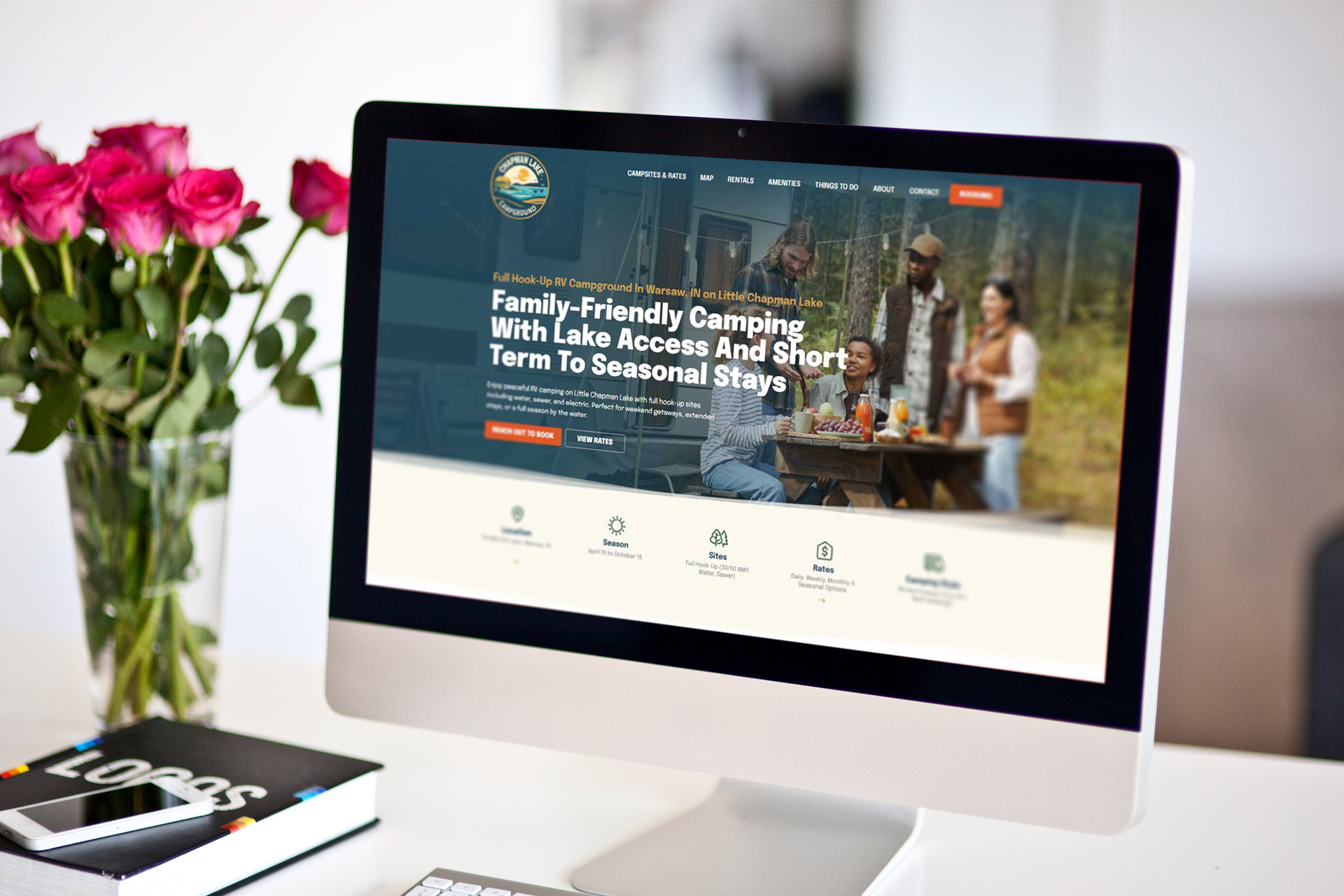Computer screen showing a camping website, with roses and a notebook nearby.