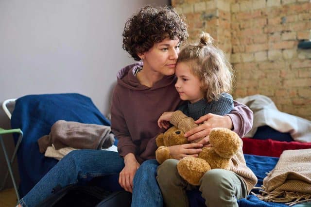 Woman and child on bed at City Mission of Findlay, cuddling a teddy bear.