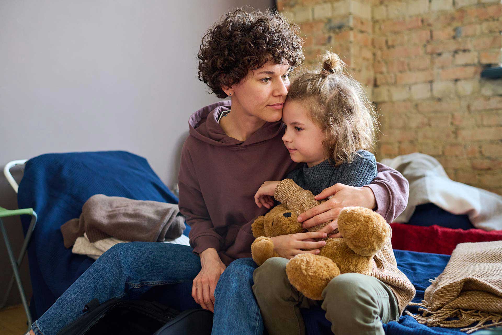Woman and child on bed at City Mission of Findlay, cuddling a teddy bear.