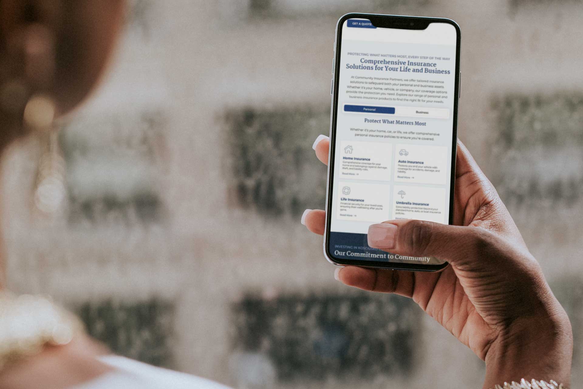 Hand holding a smartphone showing Community Insurance Partners webpage.