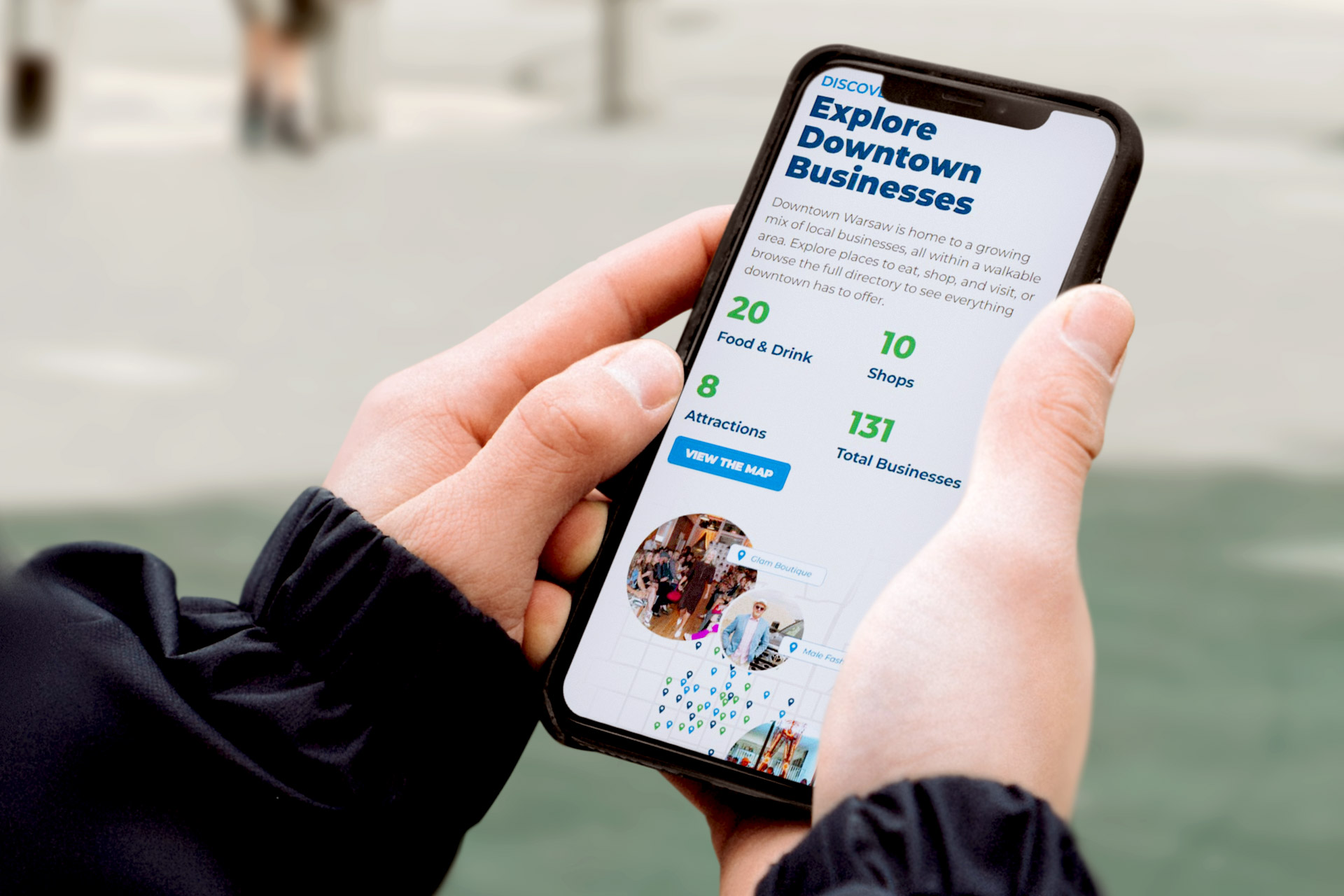 Person holding a phone displaying a webpage about downtown businesses and a map.