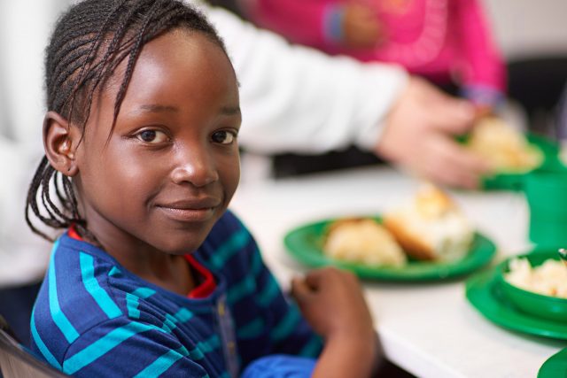 Child in a blue striped shirt sits at a table with a meal on a green plate.