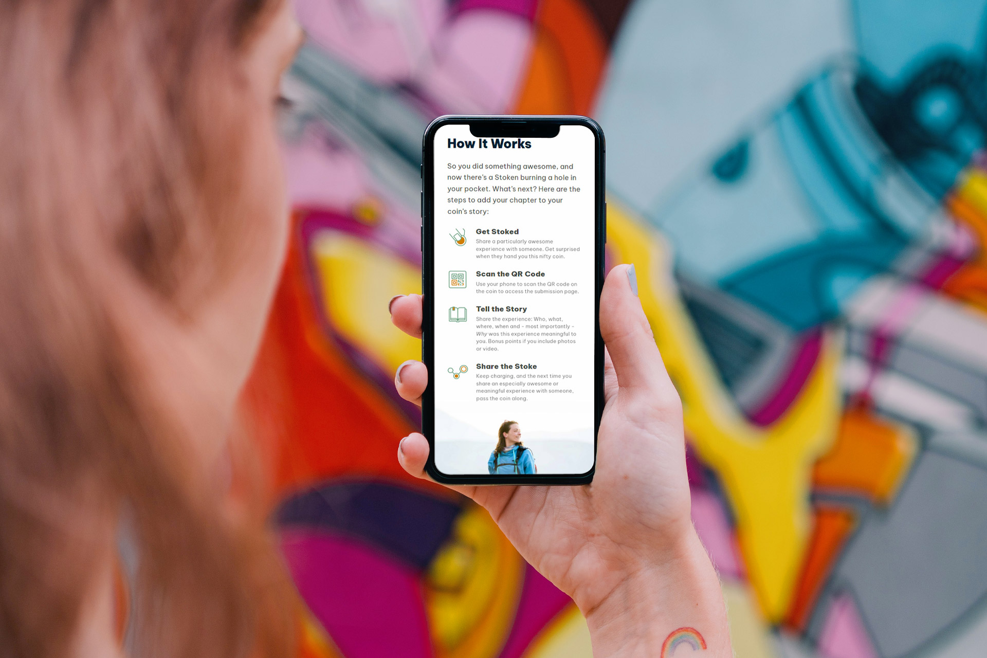 Person holding a phone displaying app instructions in front of a colorful mural.