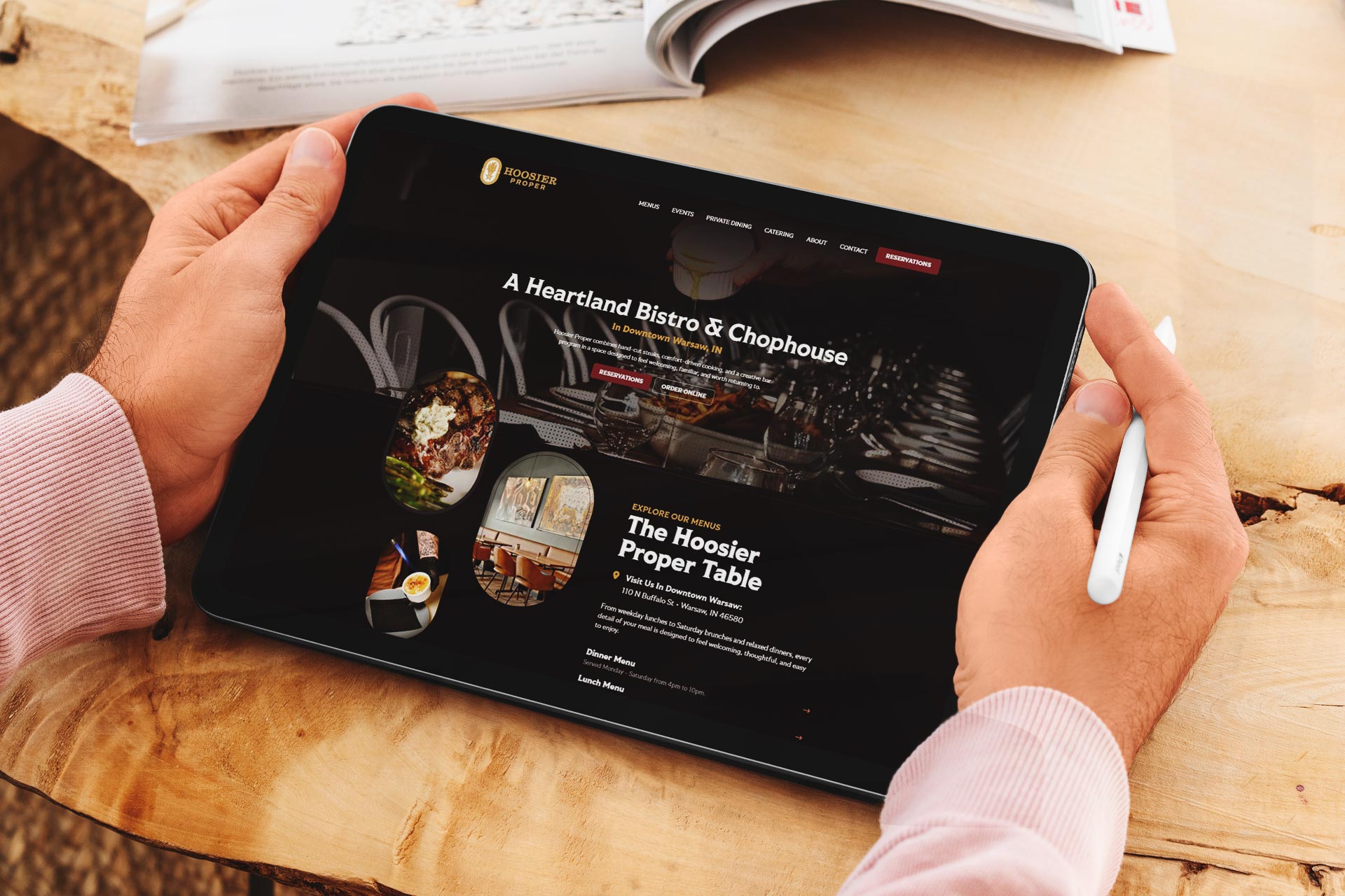 Person holding a tablet displaying a restaurant website at a wooden table.