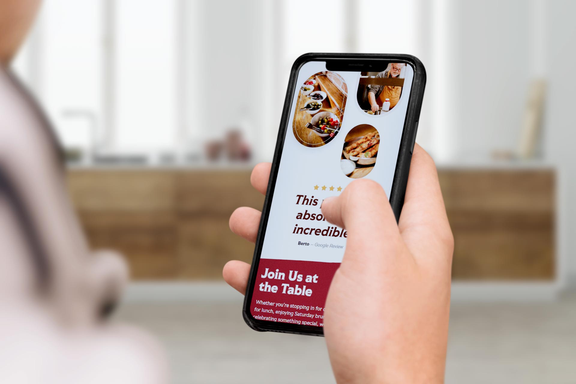 Person holding smartphone displaying a restaurant website with food images and text.