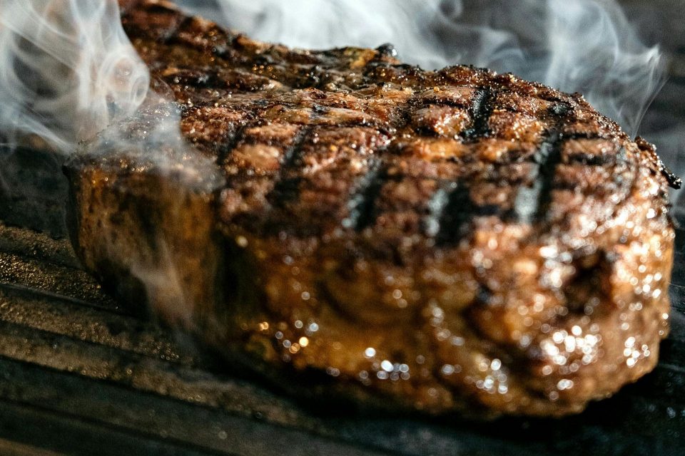 A grilled steak with char marks and visible smoke rising from it on a grill.