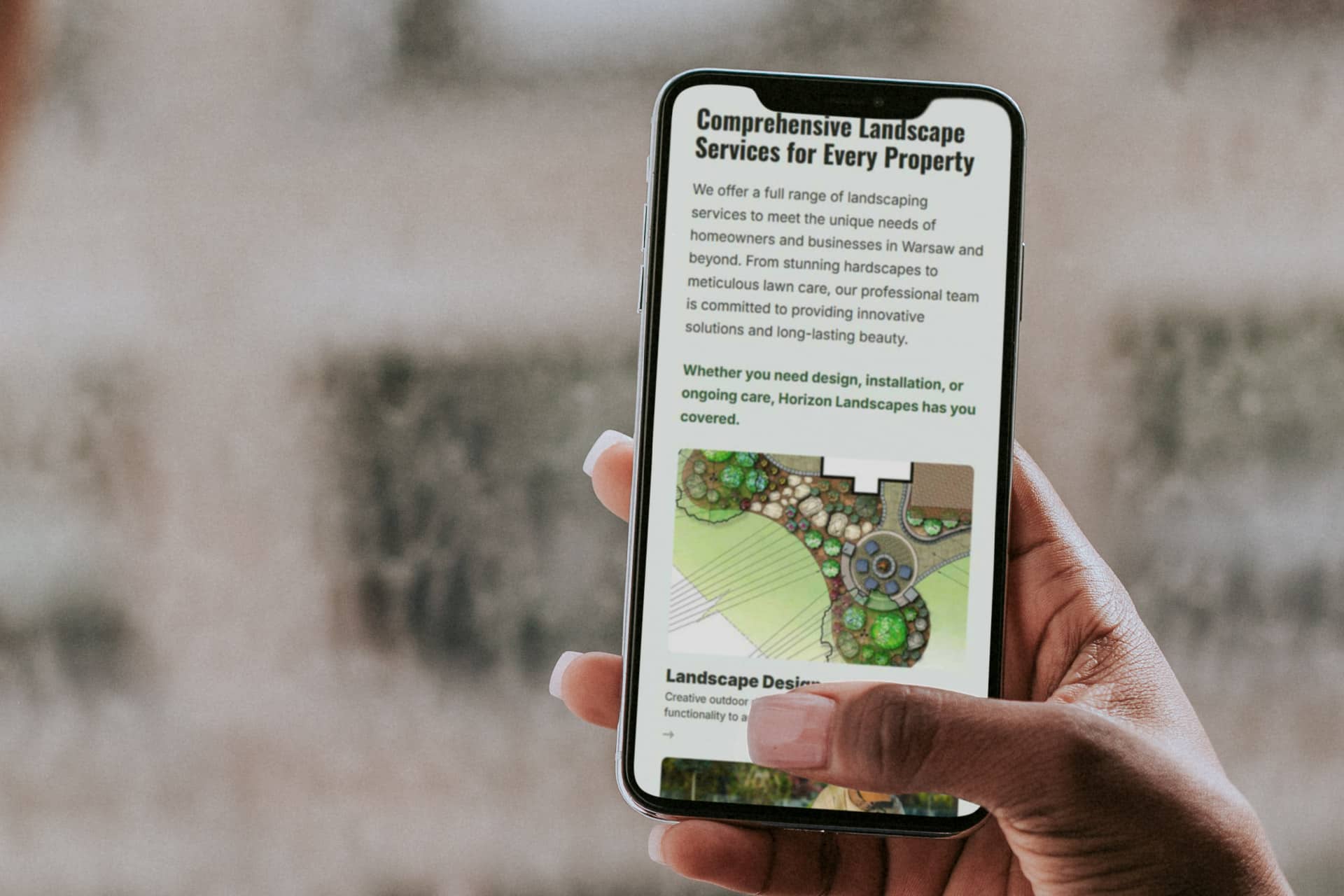 Hand holding a smartphone showing Horizon Landscapes website.