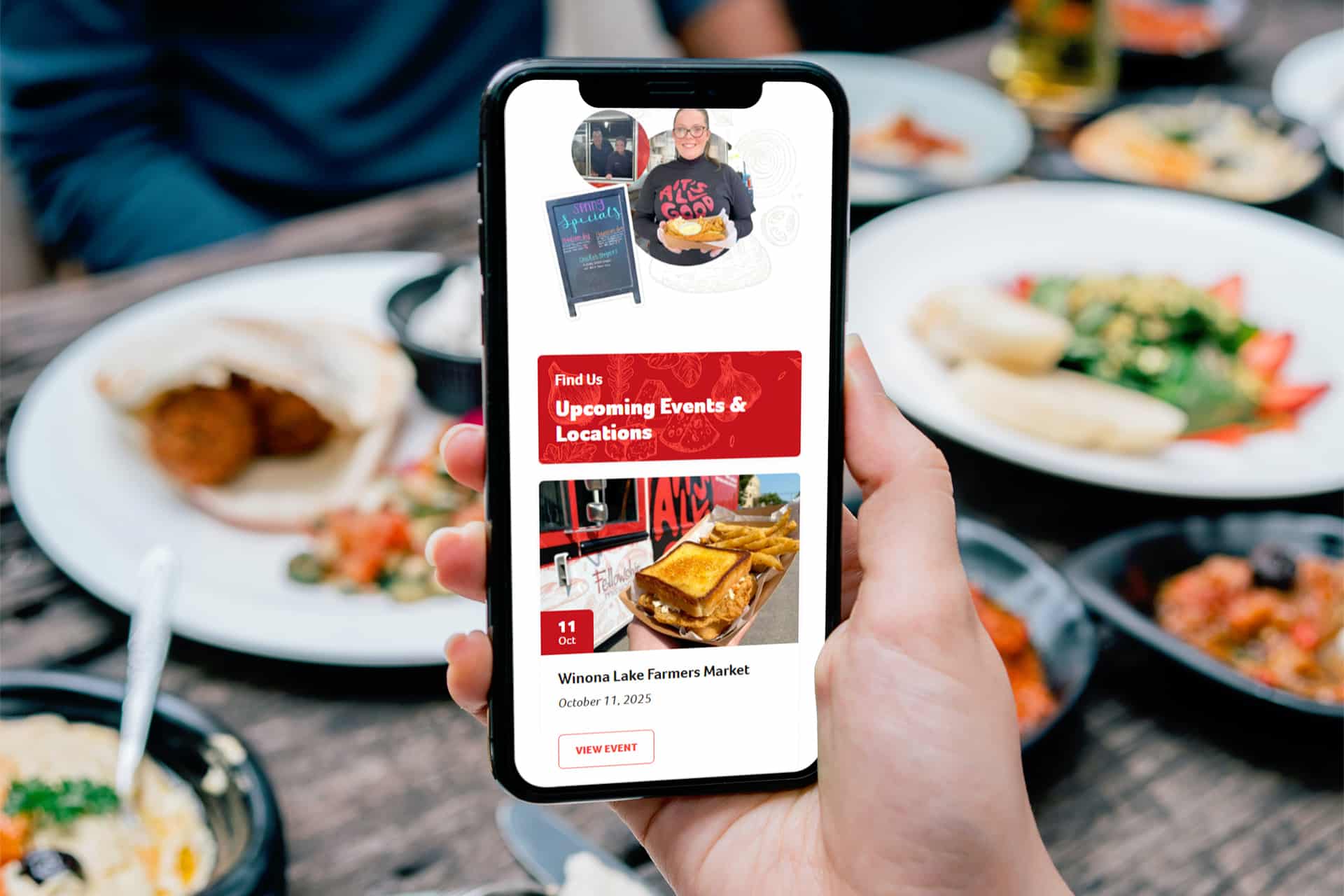 Person holding phone showing an event listing app at a table with plates of food.