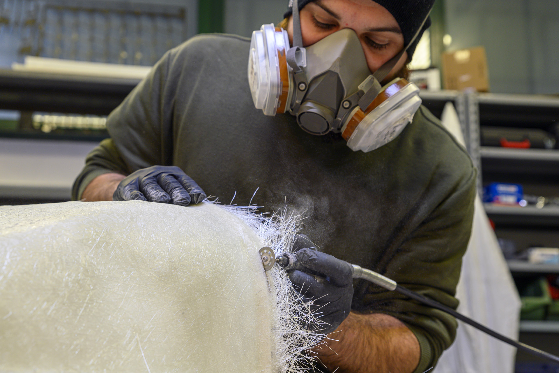 Person wearing a respirator sanding the edge of a fiberglass sheet.