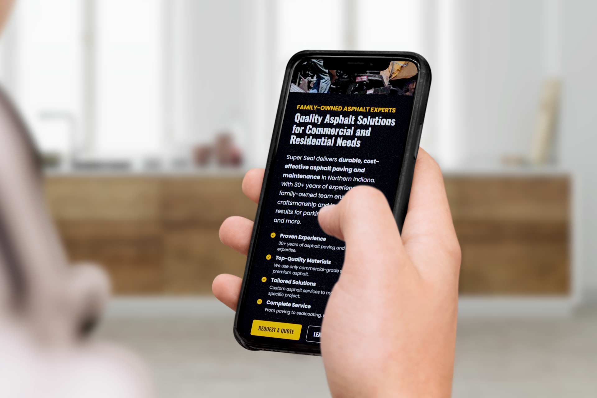 Person holding a phone showing the Super Seal asphalt services webpage.