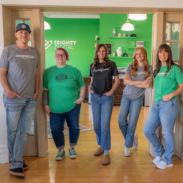 Five people stand in an office with green walls and 1Eighty Digital branding.