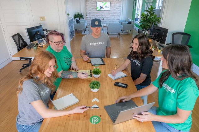 Five people discuss SEO strategies around a conference table with laptops.
