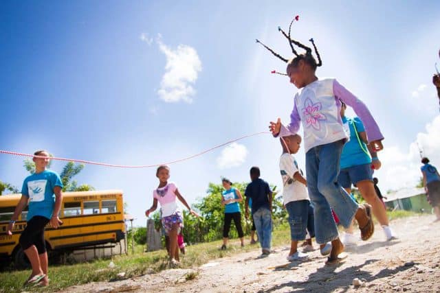 Children joyfully playing jump rope outside on a sunny day near a 2nd Mile Missions bus.