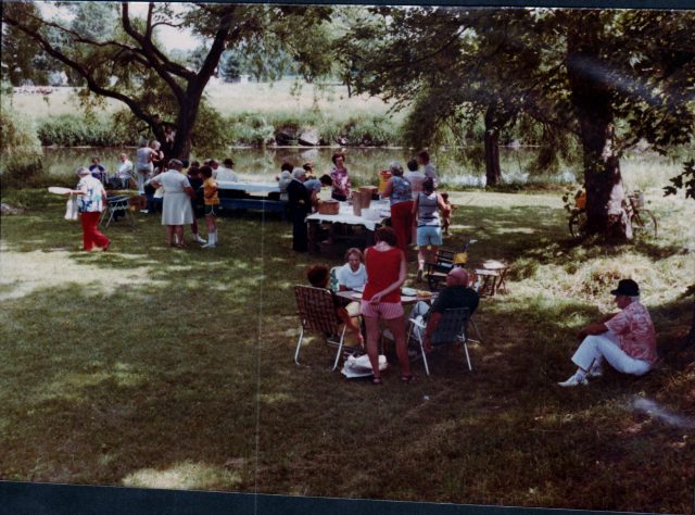 People gathered for a picnic under trees near a river in Kosciusko County.