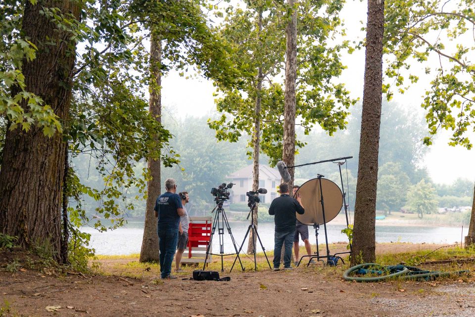 Film crew by a lake, surrounded by trees, capturing magic for DreamOn Studios.