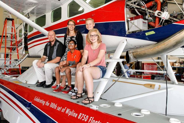 Five people sitting on a floatplane in a hangar.