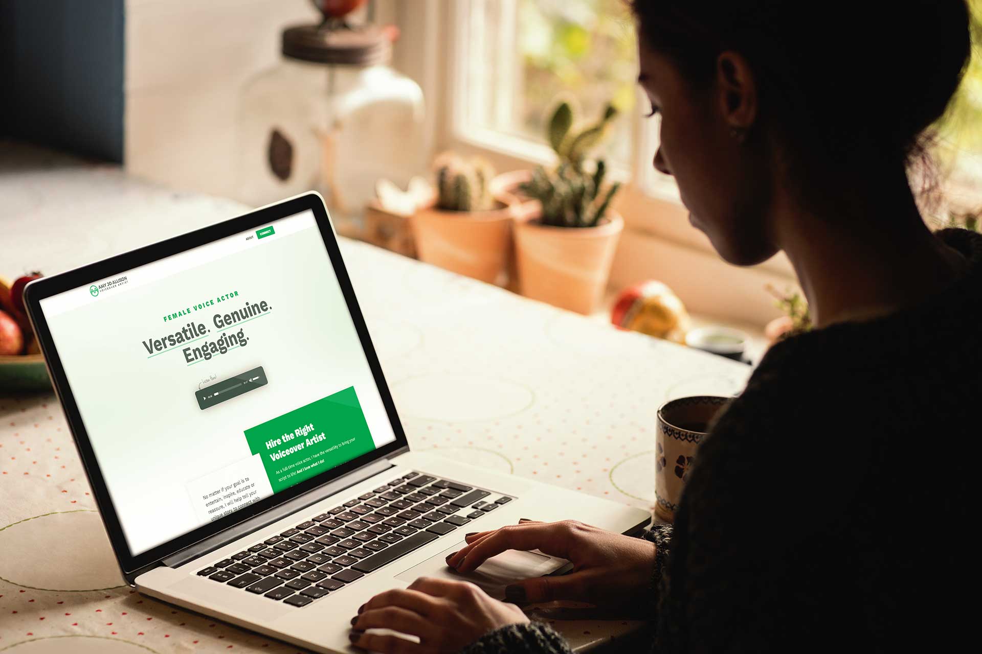 Person using a laptop at a table with plants and a mug nearby.