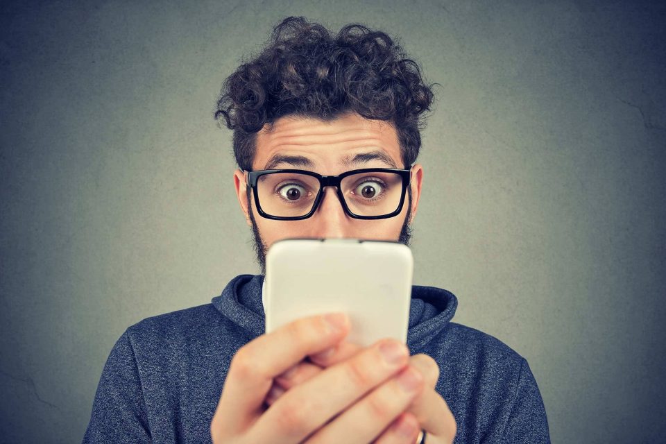 Person with glasses, surprised by smartphone screens marketing services.