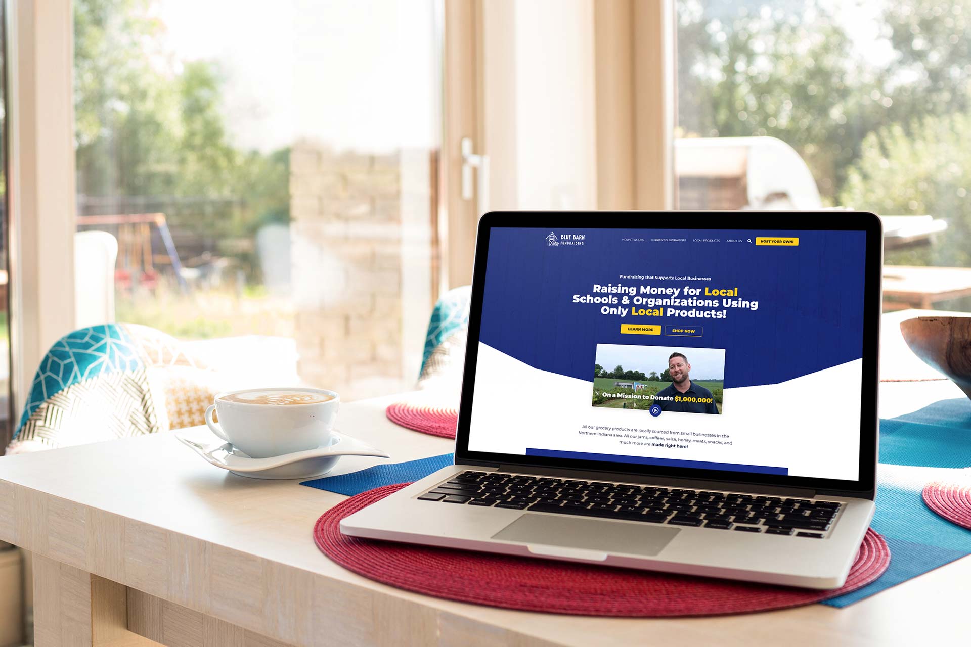 Laptop on table with a blue barn fundraising website and coffee cup nearby.