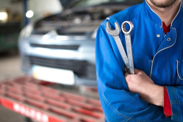 Mechanic from Boggs Automotive with wrenches near a car in a garage.