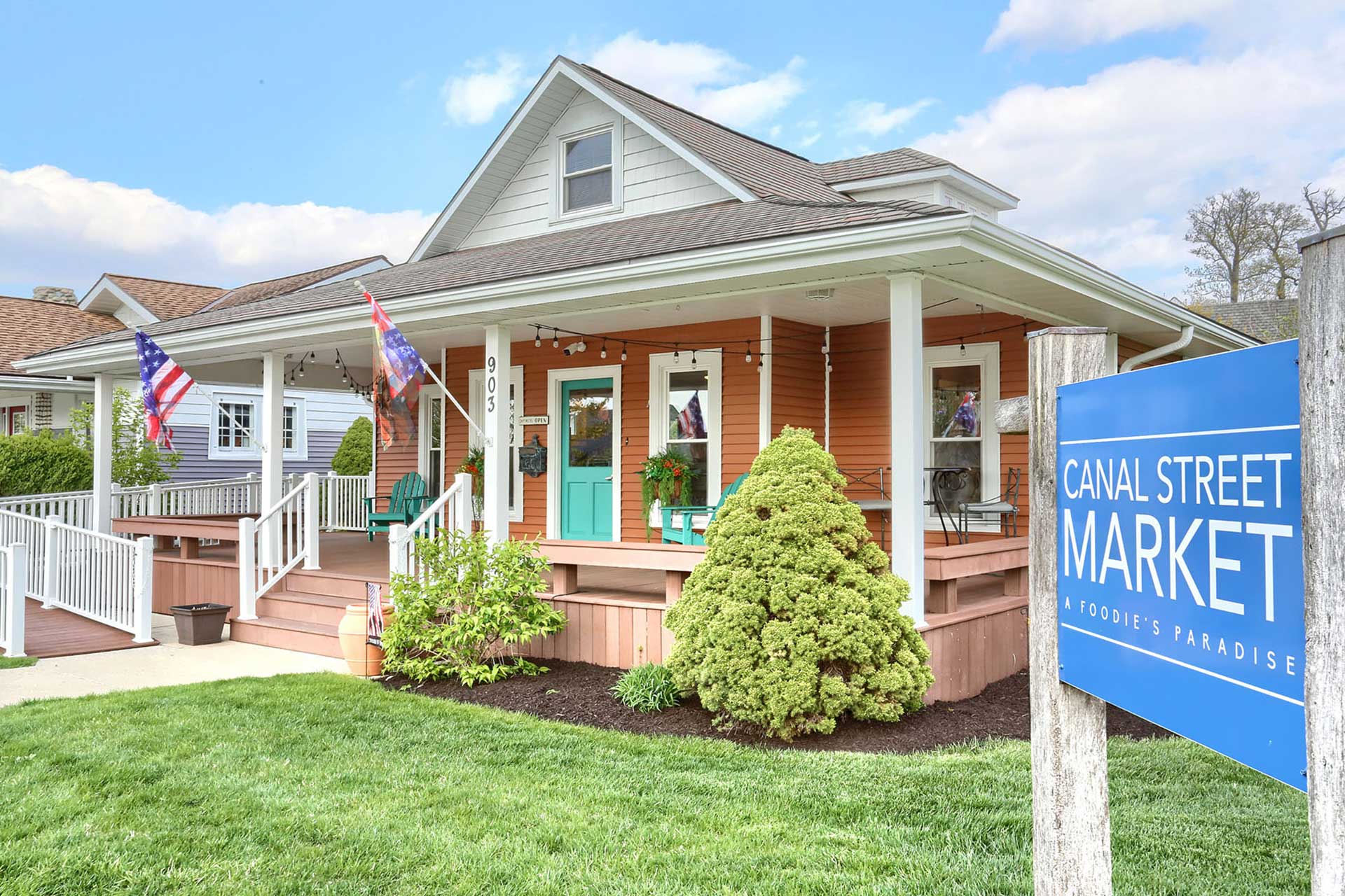 Bungalow-style house with flags, porch, and Canal Street Market sign.