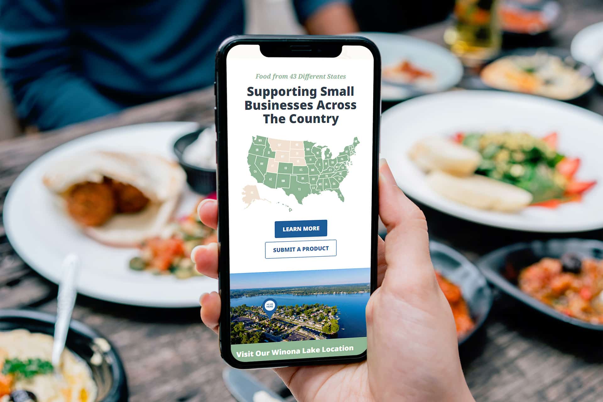 Phone displaying a small business support webpage, held over a table of food.