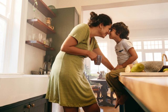 Woman and child touch noses in the kitchen, coached gently by Sally.