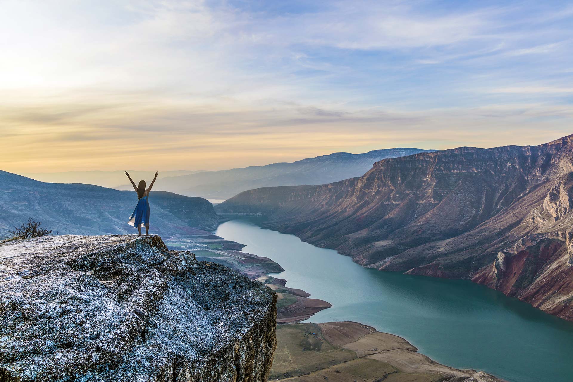 Sally coaches from a cliff, overlooking a sunrise river and mountain landscape.