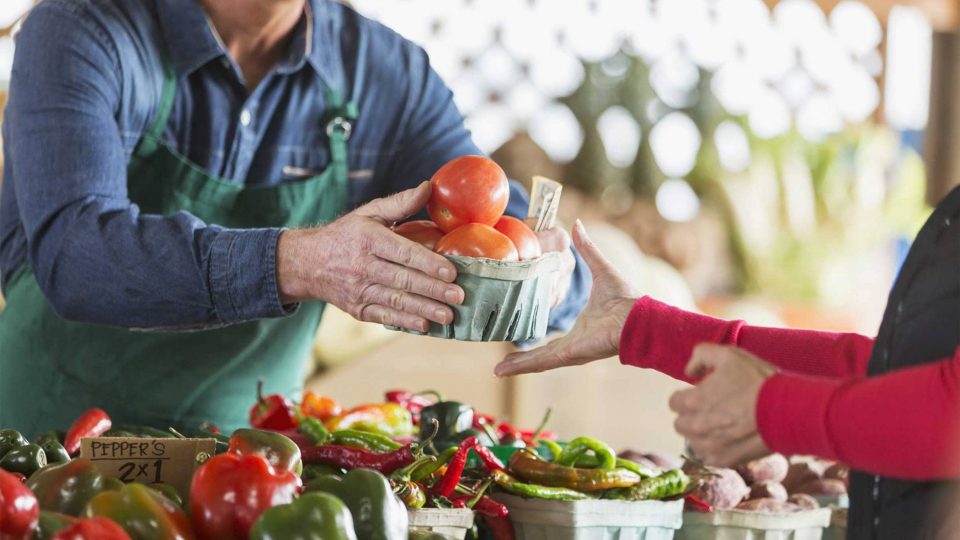 Columbia City vendor hands tomatoes to customer at a market stall.