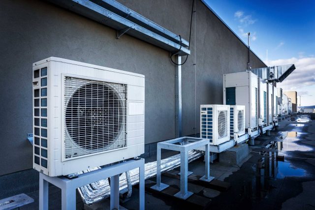 Air conditioning units on a rooftop with wet surface and cloudy sky.