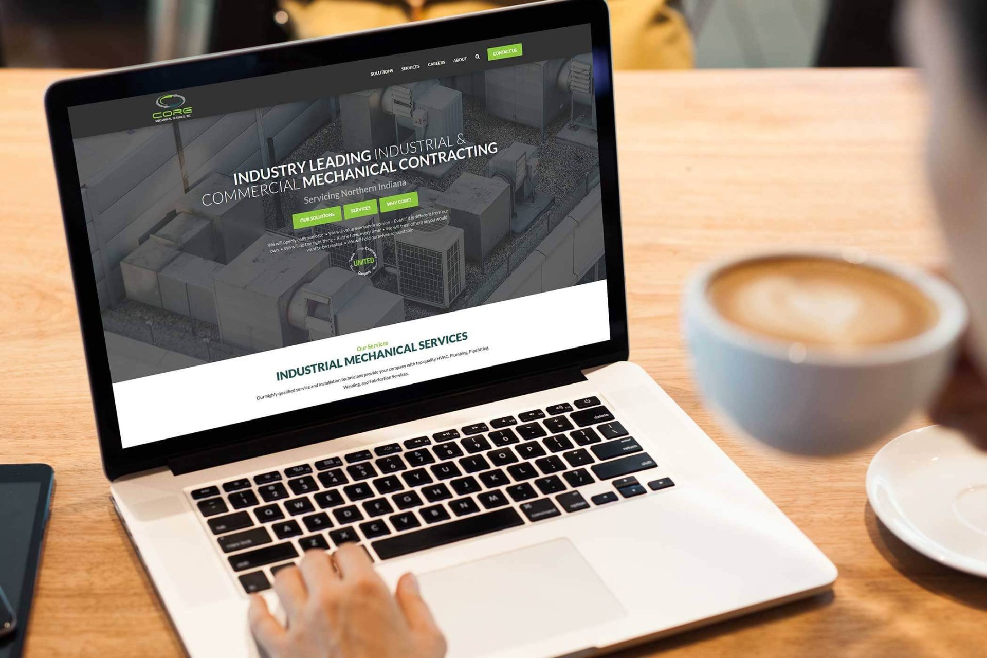 Person viewing industrial service website on a laptop while holding coffee.