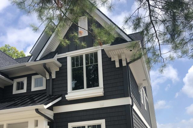 Modern house with dark siding and white trim under a blue sky.