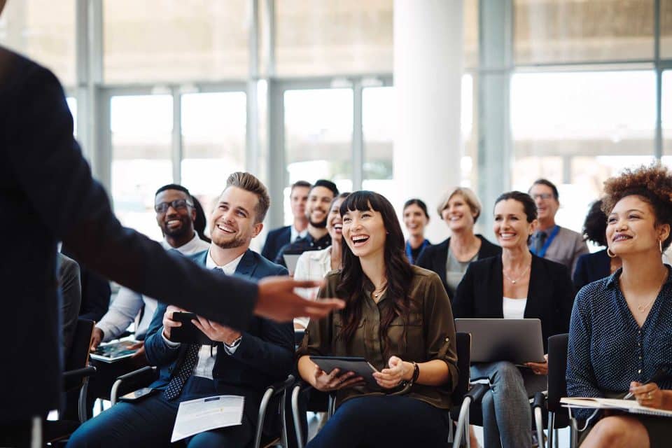 Audience smiling and clapping during EVI Training in a bright room.