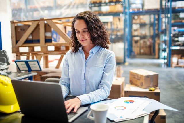 EnPak user analyzing charts on a laptop in a bustling warehouse.