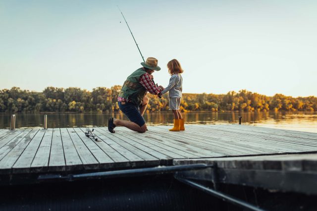 Adult and child fishing at sunset on a Fulton County lake dock.