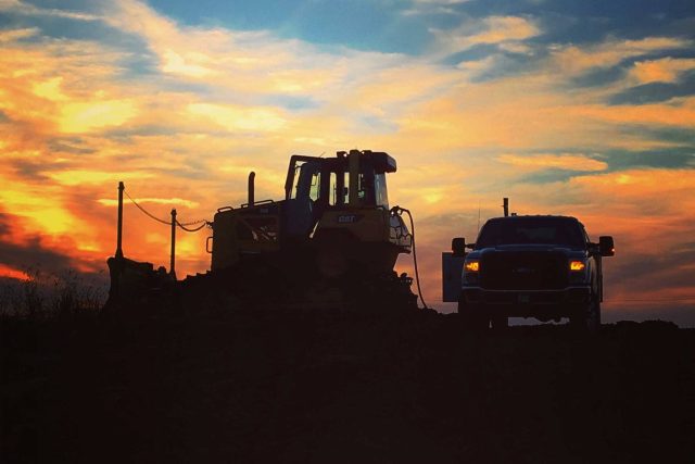 Bulldozer and truck silhouetted against a vibrant sunset sky.
