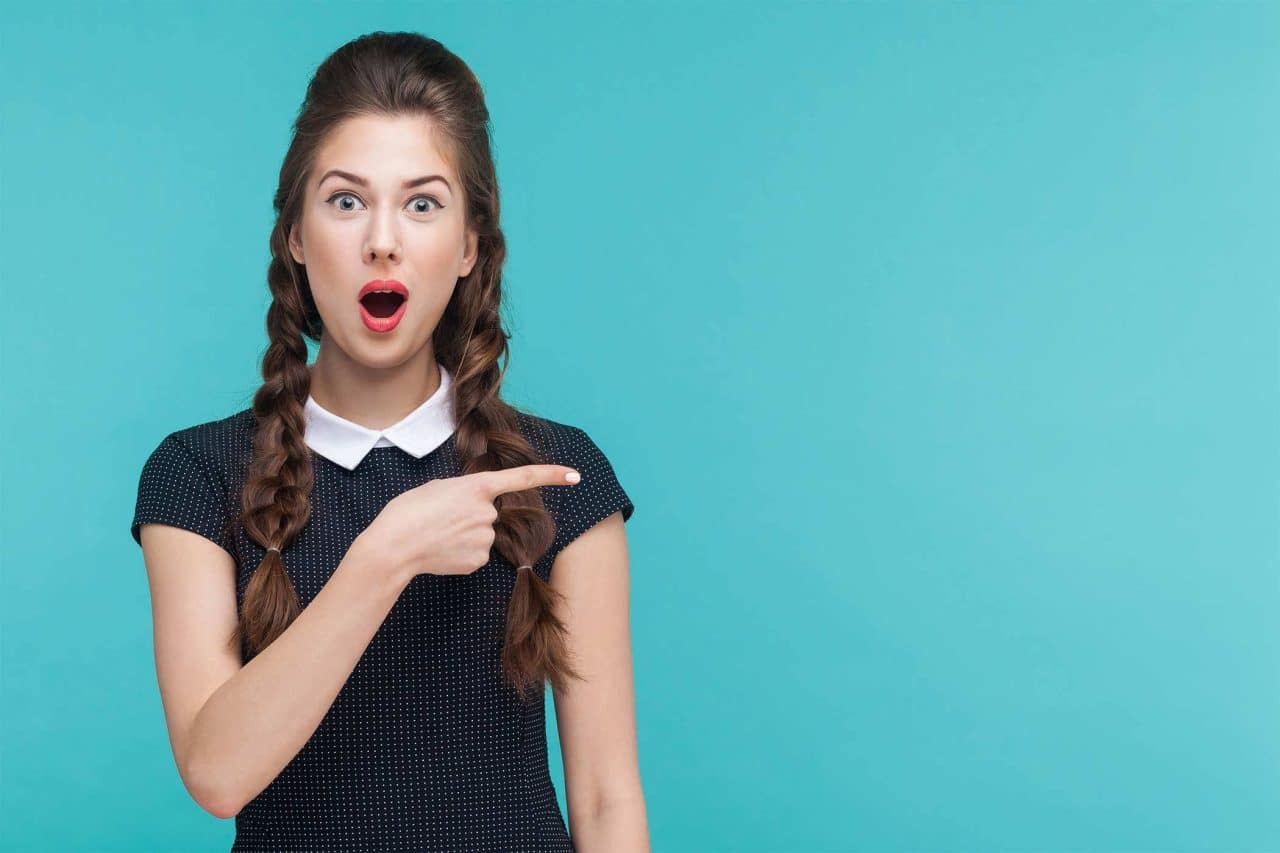 Surprised woman with braids points right, thinking of digital marketing services.