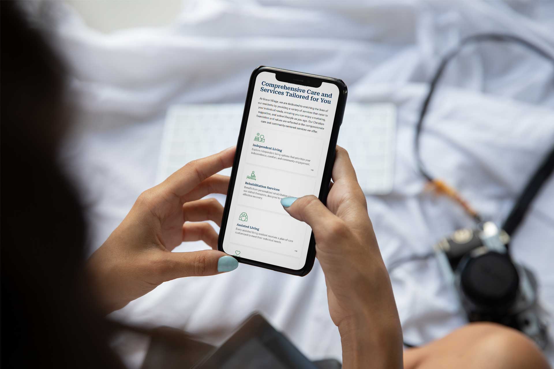Person holding a phone with Grace Village info, next to a camera on a bed.