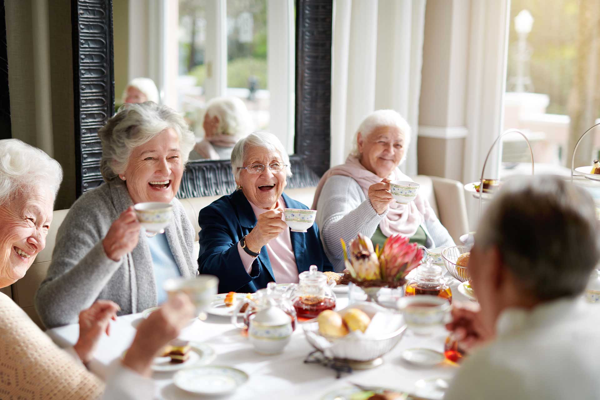Grace Village elders enjoy tea and pastries around a cozy indoor table.