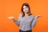 Person shrugging in a striped shirt, pondering a new website. Orange backdrop.