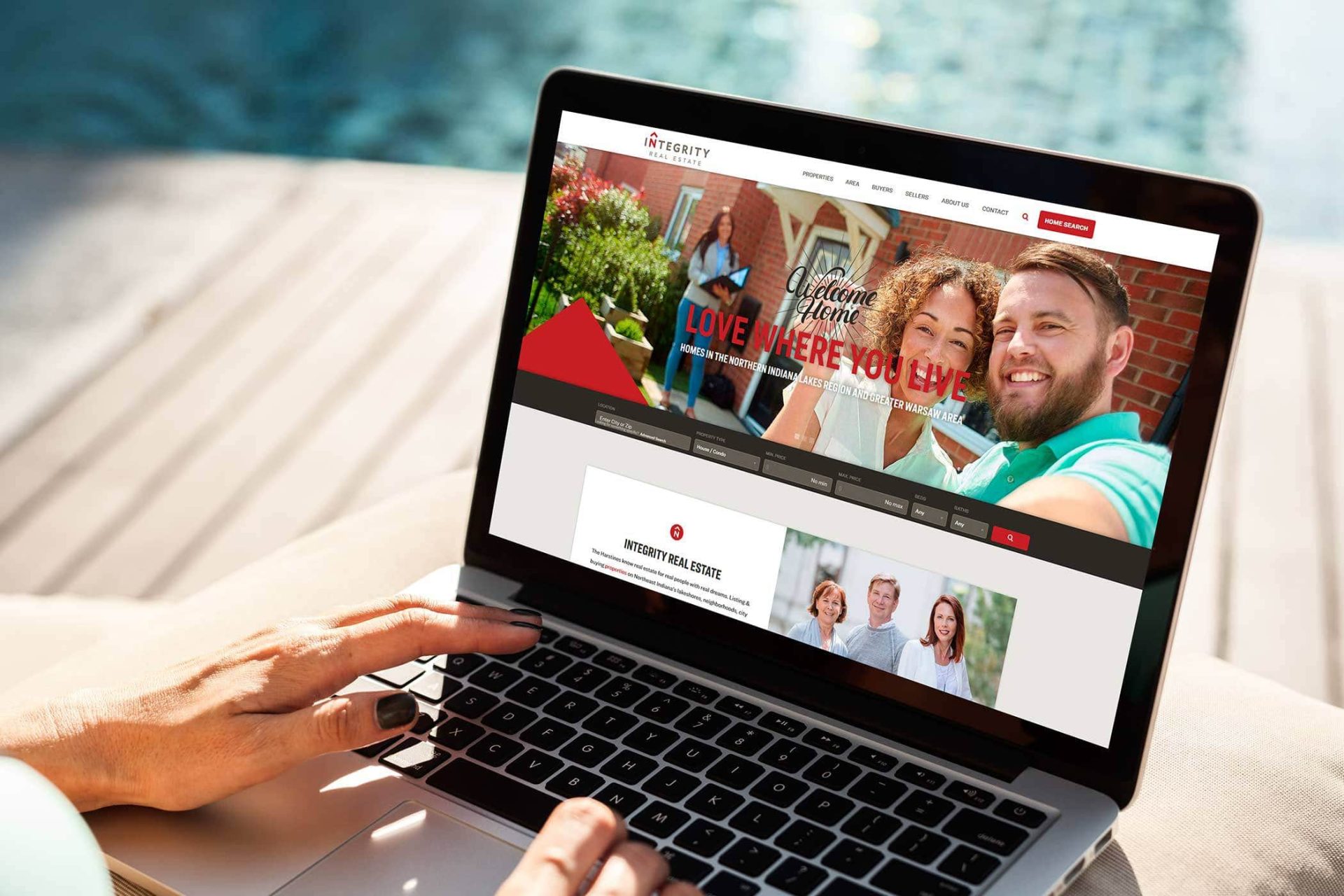Person using a laptop displaying a real estate website by a pool.