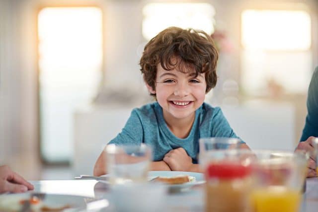 Smiling child sitting at a table with breakfast items.
