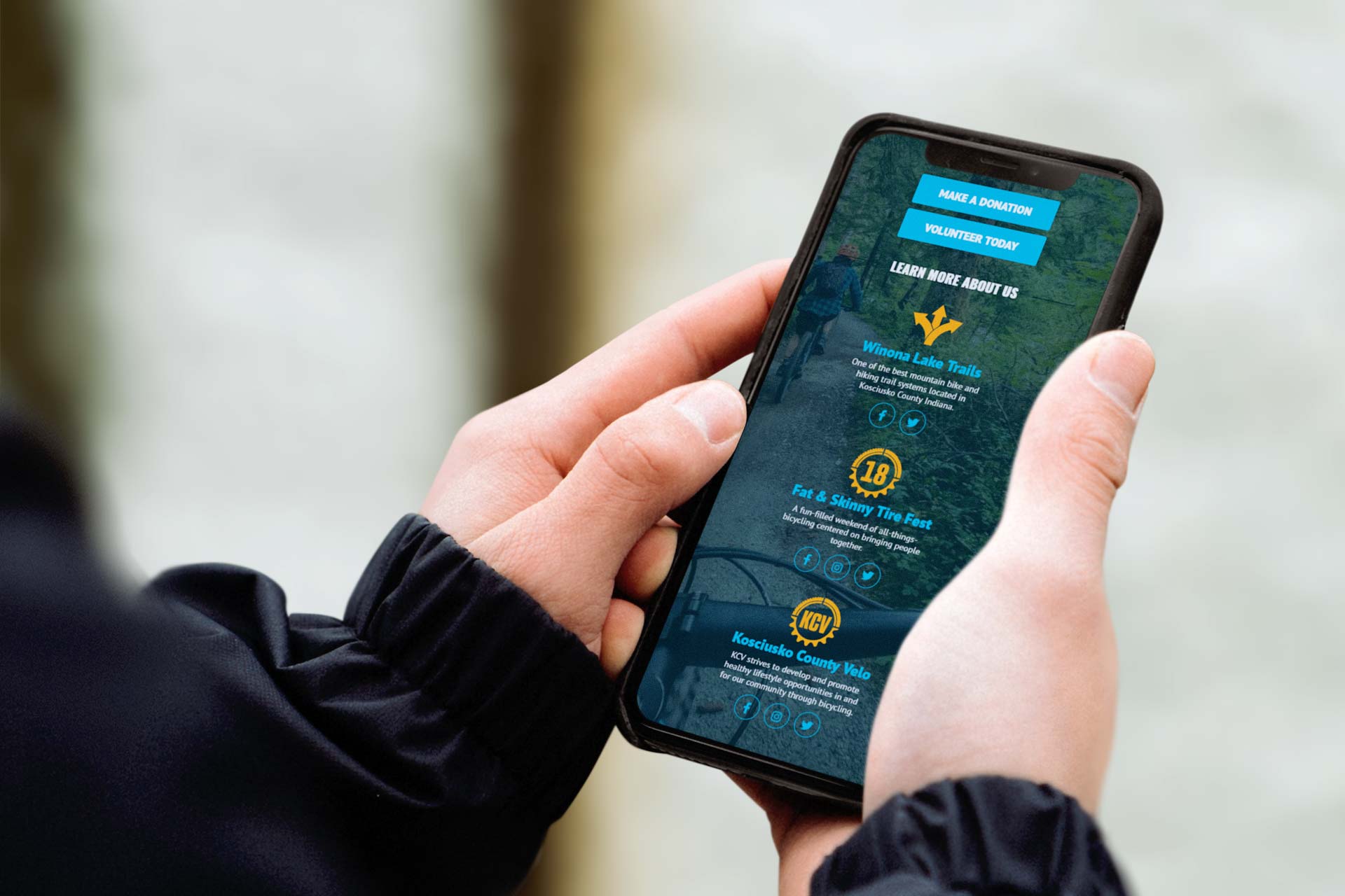 A person holds a smartphone showing Kosciusko County Velos volunteer options.