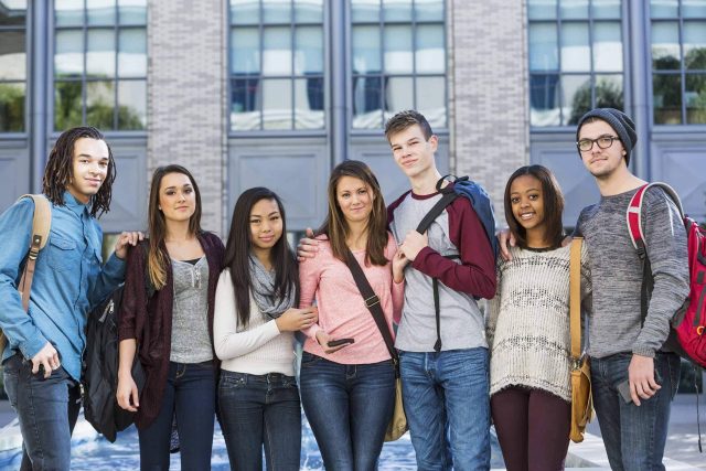 Group of seven young adults standing outdoors with backpacks.