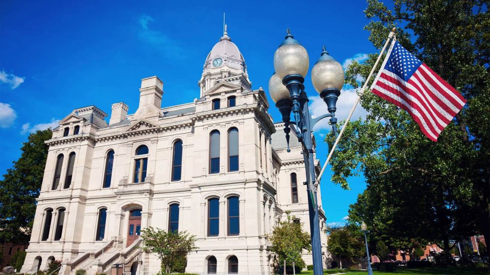 Kosciusko County courthouse, flag, and lamp post on a sunny day.