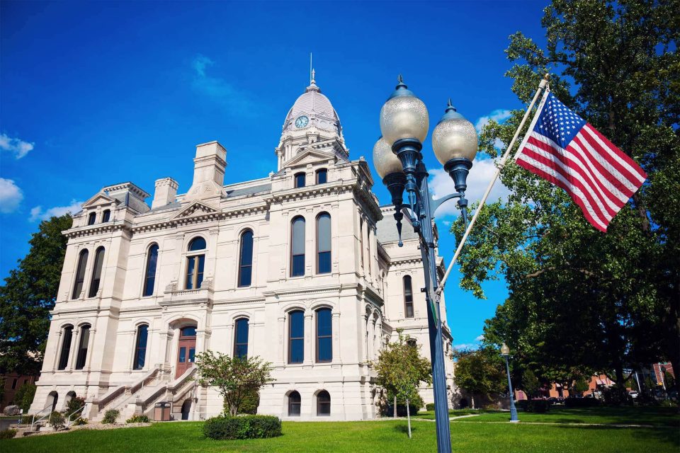 Kosciusko County courthouse, flag, and lamp post on a sunny day.